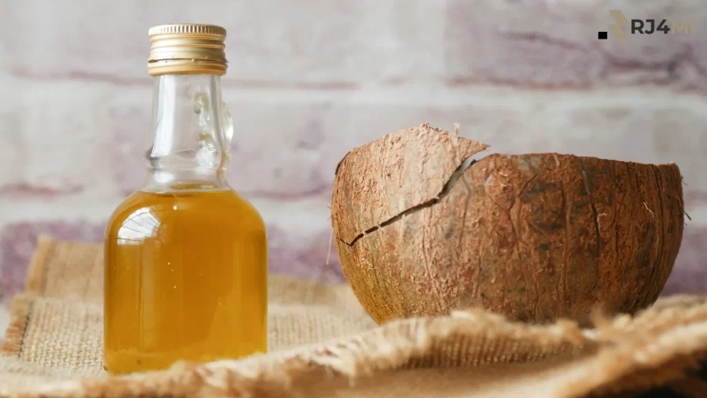 Coconut oil in a small glass bottle next to a cracked coconut on burlap fabric.