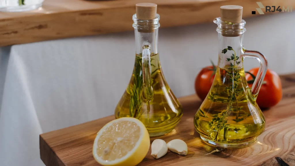 Herb-infused oil in two bottles with garlic, lemon, and tomatoes on a wooden table.