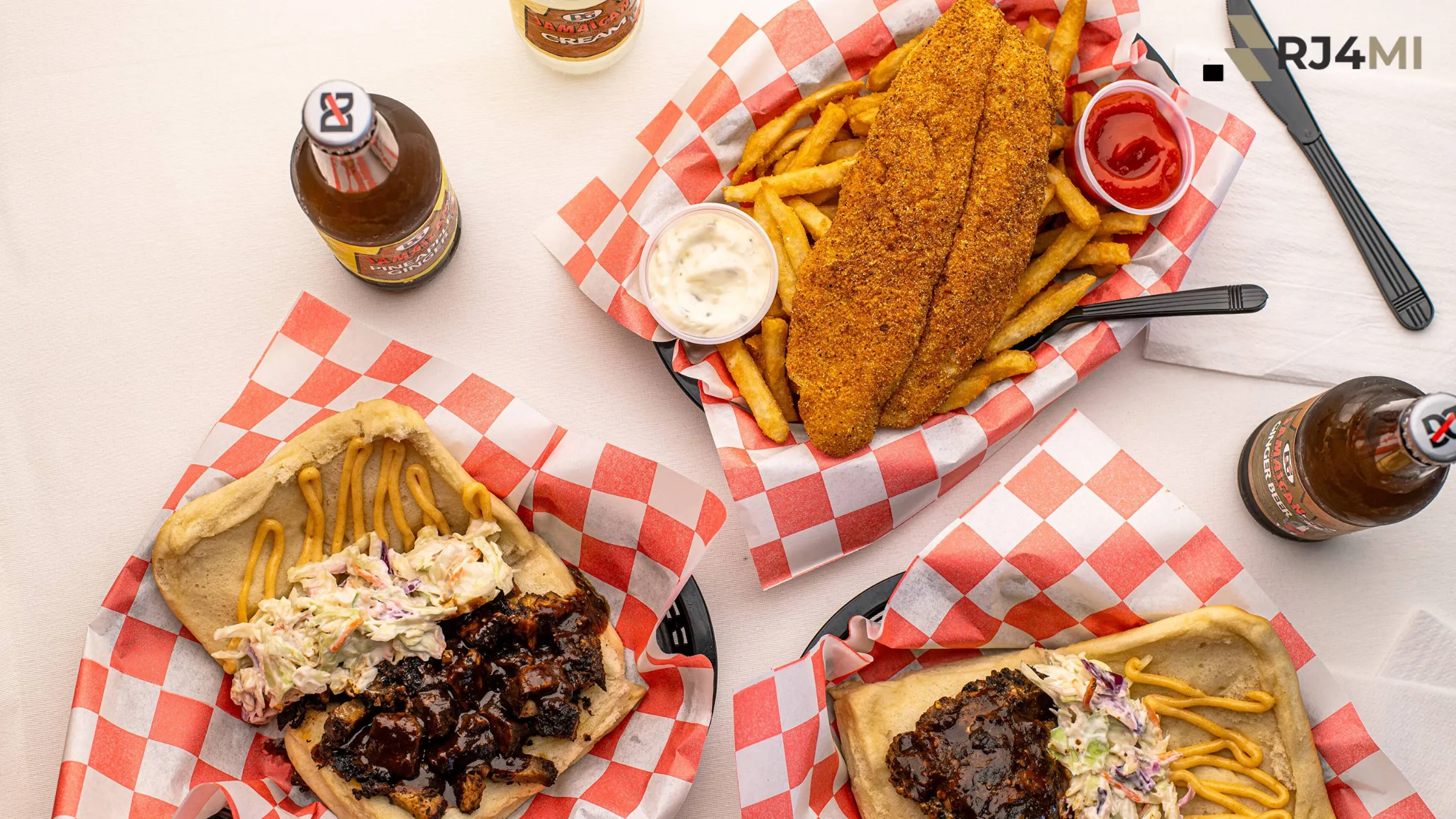 A meal featuring fried fish, BBQ sandwiches with coleslaw, mustard, and fries on a checkered paper tray.