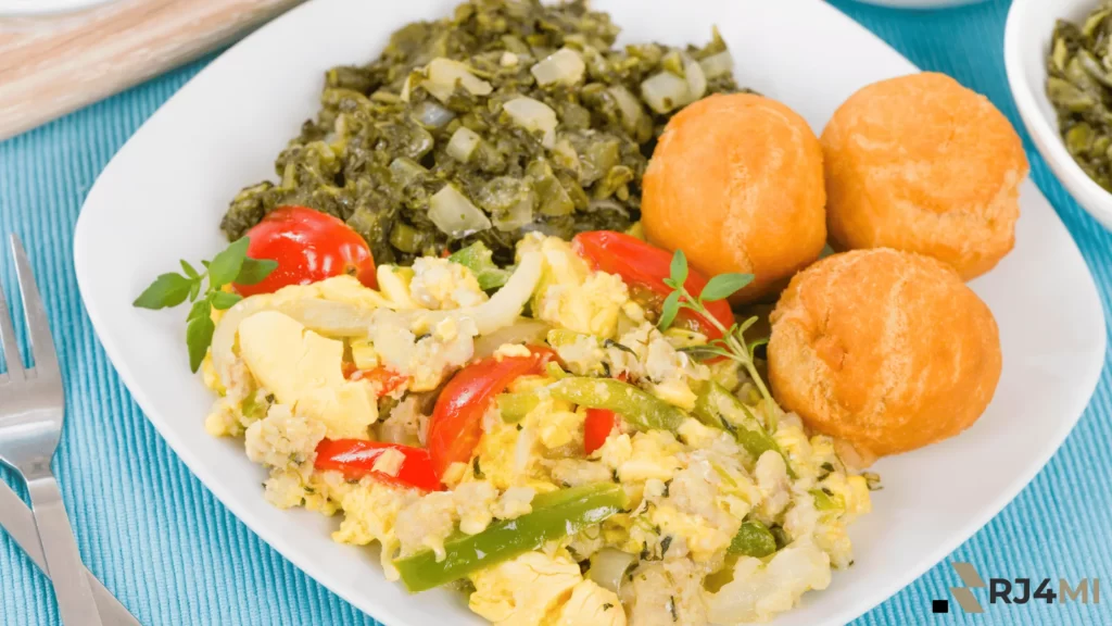 A plate of ackee and vegetables with fried dumplings and callaloo, served on a white plate.