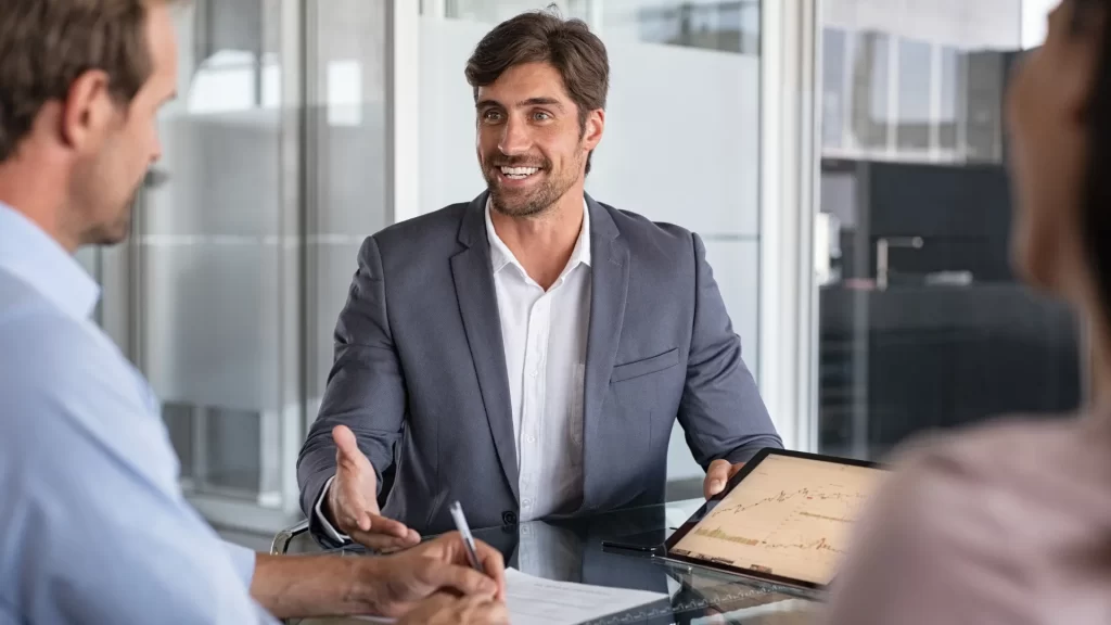 A male educational consultant discussing trends in pay with clients, showing data on a tablet. Showing as educational consultants pay wendy davison