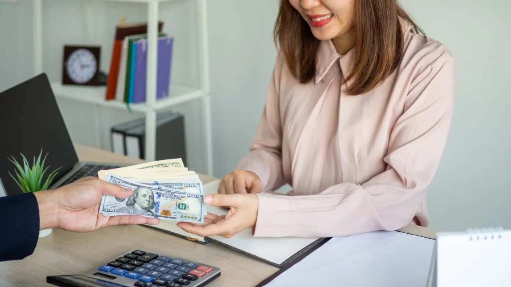 A lender handing cash to a borrower, emphasizing the financial benefits for the lender in lending transactions. 